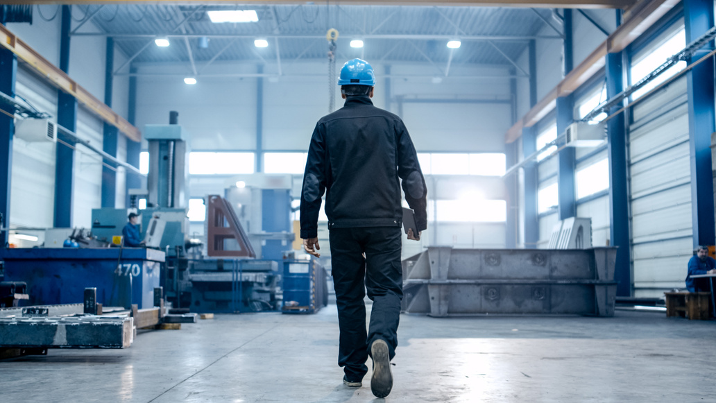 Factory worker in a hard hat is walking through industrial facilities.